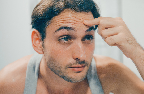 Mann im Spiegel betrachtet seine Stirnfalten