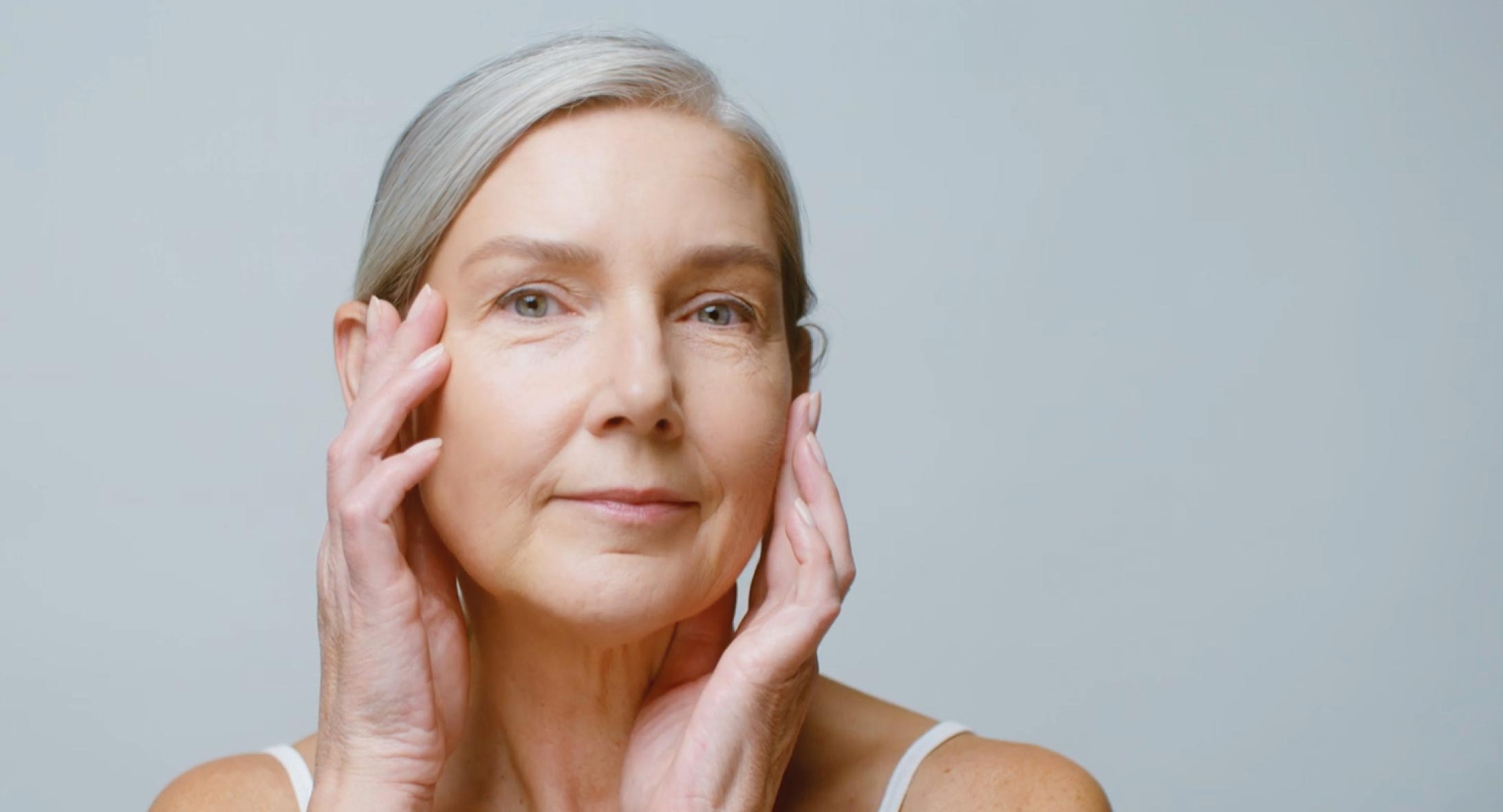 Ältere Frau begutachtet ihre Haut und ertastet Veränderungen im Gesicht | Hautpflege Menopause reife Haut | Merz Aesthetics